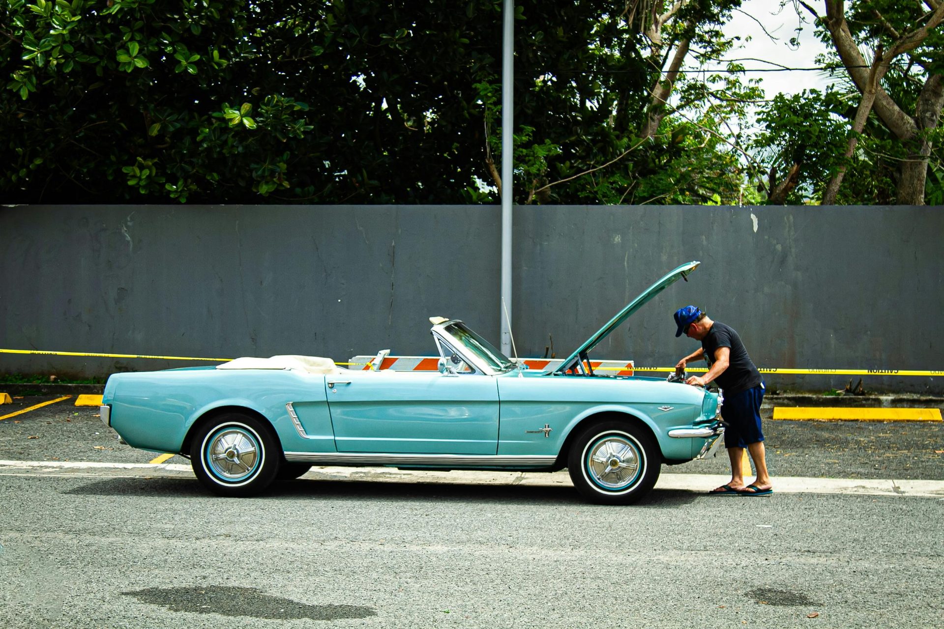 Ein Mann begutachtet ein blaues Oldtimer-Cabriolet, das an einer Straße geparkt ist – eine klassische, nostalgische Szene unter freiem Himmel.